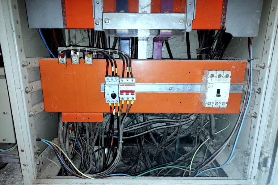 Parte inferior de um painel elétrico com dezenas de cabos empilhados e entrelaçados abaixo da régua de disjuntores.